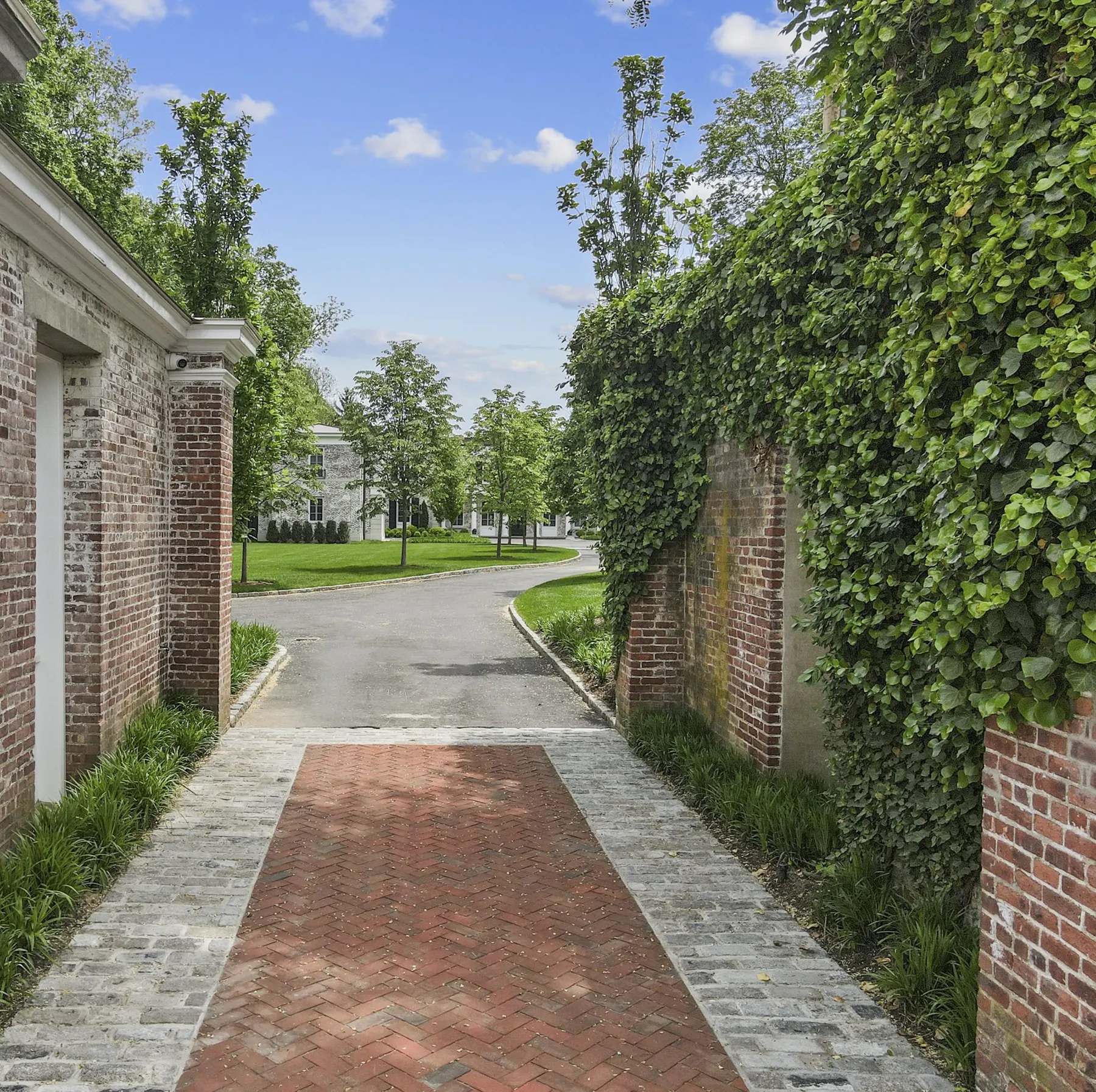 A herringbone brick walk between old brick walls covered in ivy