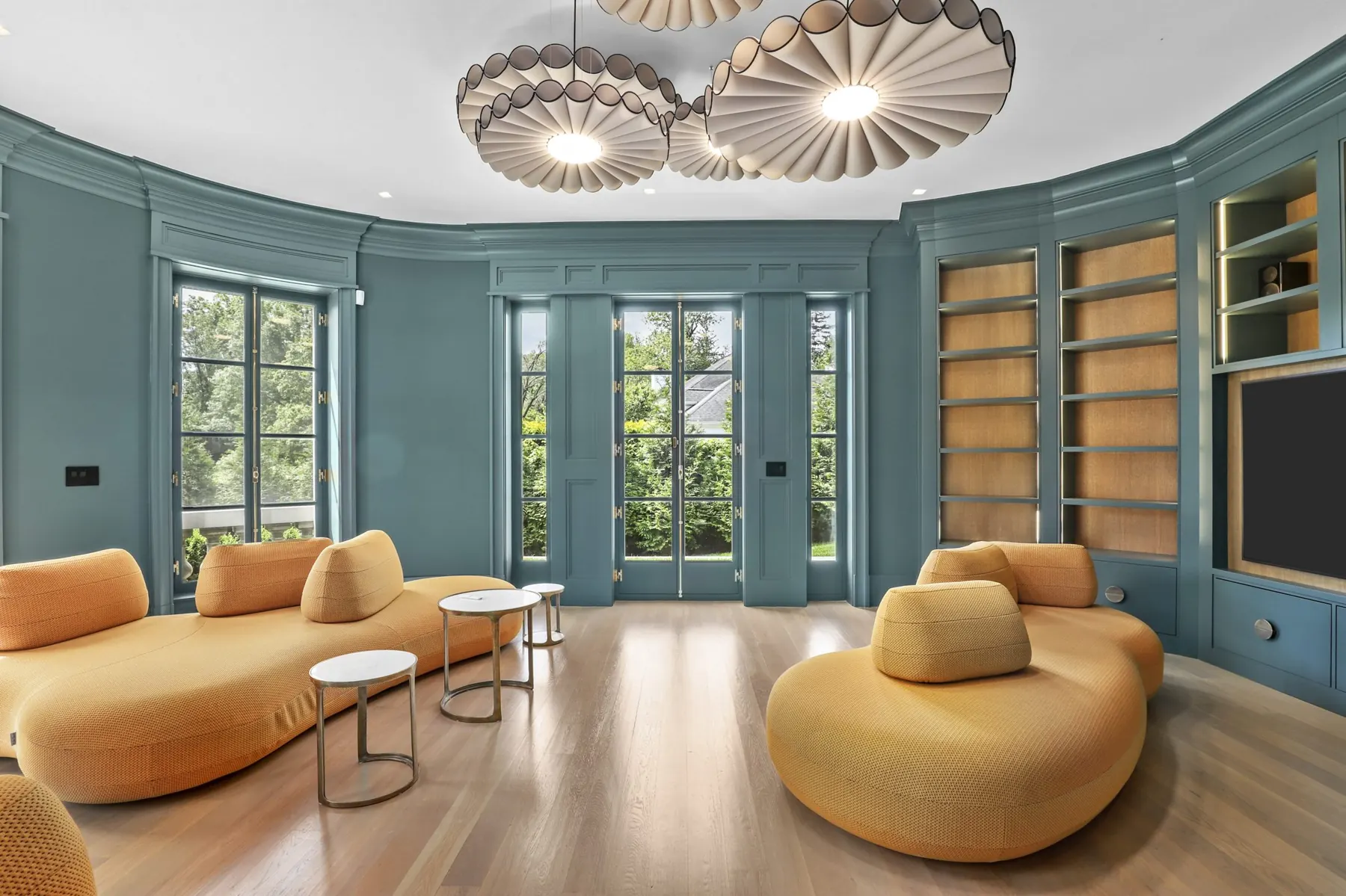 A curved, teal-painted paneled library with built-in shelving and French doors